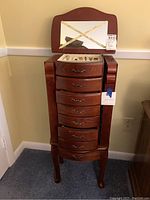 Front view of the wood jewelry armoire showing the overall piece with mirror lid and drawers.