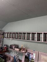 Side view of the 24-foot aluminum extension ladder and the 15-foot wooden ladder hanging horizontally on a garage wall above various household items.
