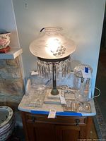 Main view of frosted glass lamp illuminated on marble-top table with clear glass lamp and extra crystals in front.