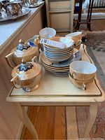 Full view of luncheon set on wooden table including stacked saucers, cups, and covered containers.