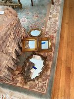Four decorative framed mirrors displayed on a floral area rug next to patterned fabric furniture. Shows variation in shapes and frame styles.