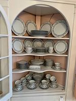 Wide view of white china with pastel floral pattern in display cabinet. Plates, bowls, cups, and serving pieces arranged on shelves.