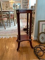 Full view of the plant stand showing dark wood frame, four slender legs with gold accents, and the tripod base design.