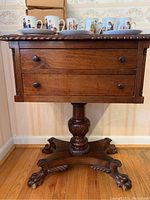 Full frontal view of the wooden side table showing two dovetailed drawers and the twisted rope design on the edge of the tabletop with some decorative cups on top.