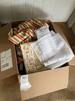 Box of assorted linens with striped cloth and white lace linens on top