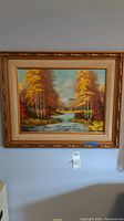 Full image of the framed oil painting depicting autumn landscape with river and trees