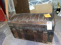 Front and side view of the antique wooden steamer trunk showing embossed metal bands, leather straps, and rivets.