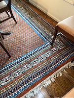 Area rug on hardwood floor under dining chairs showing overall pattern and border design with white fringe.