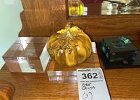 Three Asian art glass pumpkin sculptures on clear square bases, showing detail of glass leaves and stems.