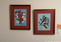 Two framed paintings hung on wall, the left one floral and the right one bird, both signed by R Hinden and framed in wood gold-tone frames with red matting and blue background in painting area