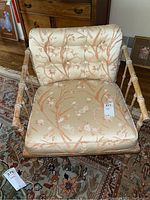 Front view of chair showing fabric seat and back cushions with a floral and butterfly pattern, wooden faux bamboo frame visible.