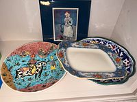 Four decorative plates stacked with a colorful hand-painted style plate on the left and three floral bordered plates on the right.
