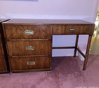 Front view of Dixie brand wooden desk showing three large drawers on the left with metal recessed handles and one smaller drawer on the right supported by grooved wooden legs.