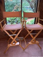 Two tall director chairs side by side showing wooden frames and light pink fabric seats and backs.