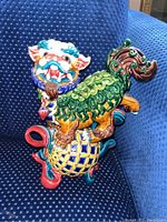 View of one colorful Asian ceramic mythical figurine featuring a lion-like face, green scales, and standing on a multi-colored checkered ball base with red curved feet.