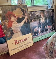 Photo showing two framed posters against a window: Renoir poster left with a couple dancing, Manet poster right with a bar scene.