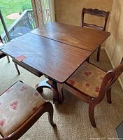 Photo showing the game table with folded rectangular burled wood veneer top and part of two chairs with patterned fabric seats.