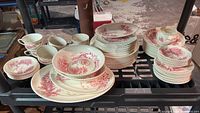 Overall view of multiple pieces of Johnson Bros red transferware ironstone dinnerware set with varied plates, cups, bowls and serving pieces stacked and arranged.