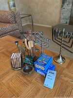 Photo showing various Judaica items including two menorahs, wooden statue, wooden Torah replicas, Chanukah candles, and small vessels arranged on a wooden table.