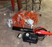 Photo showing the Homelite leaf blower, orange and white extension cords, white power strip, and Campbell Hausfeld battery compressor on concrete floor.
