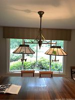 Full view of East Lake 1880 dual pendant light fixture hanging over dining table with window in background.