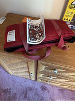 Red zippered carrying case with instruction booklet on top, placed on wooden dresser.