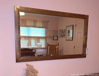 Full view of the rectangular wood framed wall mirror with brass corner accents hung on a wall.