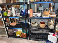 Photo of two black plastic shelving units filled with various household items (not included in lot) in a basement environment.