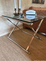 Front side view of the glass top side table with chrome metal frame placed next to a patterned couch and beige wall.