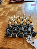 Full view of stone chess pieces arranged on the light and dark checkered marble board on parquet floor.