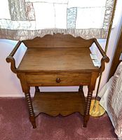 Front view showing single drawer, scalloped wood details on backboard and lower shelf, spooled legs and side handles.