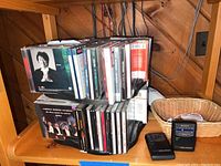 Photo of two Sony Walkman cassette players side by side with a stack of CDs on a black plastic rack near a wooden wall.
