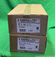 Two stacked boxes labeled Emergi-Lite Thomas & Betts exit signs model WLX1RW-C-U.