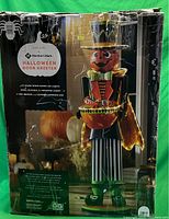 Box showing front view of 4 feet tall Members Mark Halloween door greeter with pumpkin head, colorful outfit, and 92 warm white micro LED lights.