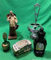 Photo showing entire lot including Mexican folk art figurine, metal spice holder, black decanter, ceramic train candle holder, and small green vase.