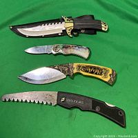 Photo of 3 hunting knives and 1 folding tree saw laid on green fabric background