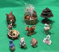 Lot of nine vintage porcelain and resin figurines arranged on green cloth background, including rabbits, birds, deer, tree, and decorative pitcher.