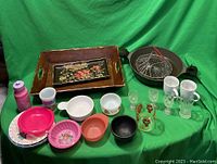Shows mixed kitchenware on a green background including frying pan, trays, bowls, mugs, and kid's plates
