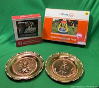 Photo of the boxed Splash Basketball Pool, boxed Brookstone Programmable Message Photo Frame, and two brass round wall hanging plates with embossed figures.