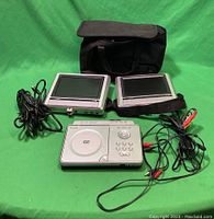 Front view of the Venturer portable DVD player main unit with two 7-inch LCD screens, connection cables, and carrying case on green background.