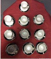 Top view of ten white ceramic teacups arranged on black floral saucers laid out on red fabric