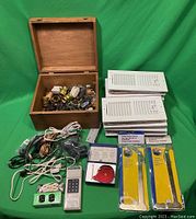Photo showing all items including wooden box filled with lamp sockets, stacked white air vent covers, electrical cords, remote control, dual outlet, red wrench, and vent brushes.