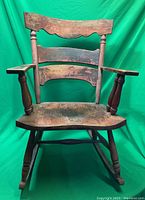 Front view of vintage wooden rocking chair showing curved back slats, armrests, and worn wood finish