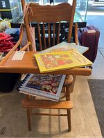 Front view of antique wooden highchair with 3 cookbooks on seat and one hanging apron on side