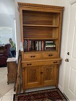 Front view of antique golden oak bookcase showing upper open shelves, two drawers, and lower cabinet with carved wooden doors. Removed glass doors and gathered hardware leaning on side.