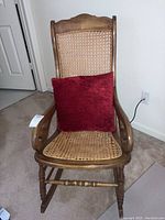 Full view of antique wood rocker with cane seat and back, red cushion placed on seat.