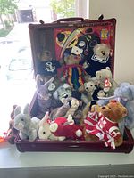 Overall group of Beanie Babies and plush animals displayed inside vintage red attach case with bright graphics