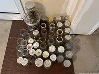 Top view of over thirty canning jars arranged on floor with lids on some jars showing variety of sizes and lid types