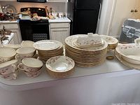 Overview of stacked plates, serving bowls, teacups, saucers and covered butter dish all with pink floral and gold trim designs.