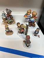 Six porcelain figurines of children in winter scenes, grouped together on surface